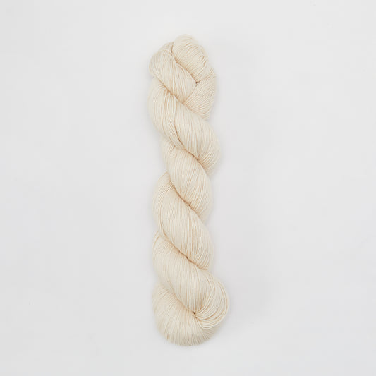 Cream-colored organic cotton yarn skein from Kinua's The Fingering collection, showcasing soft, natural fiber texture.